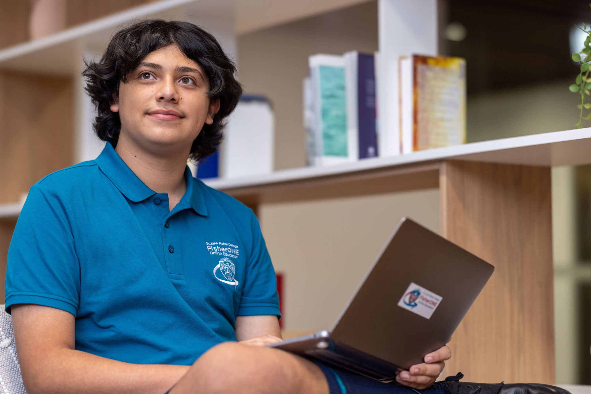 Student wearing a school polo shirt using a laptop in a learning space.
