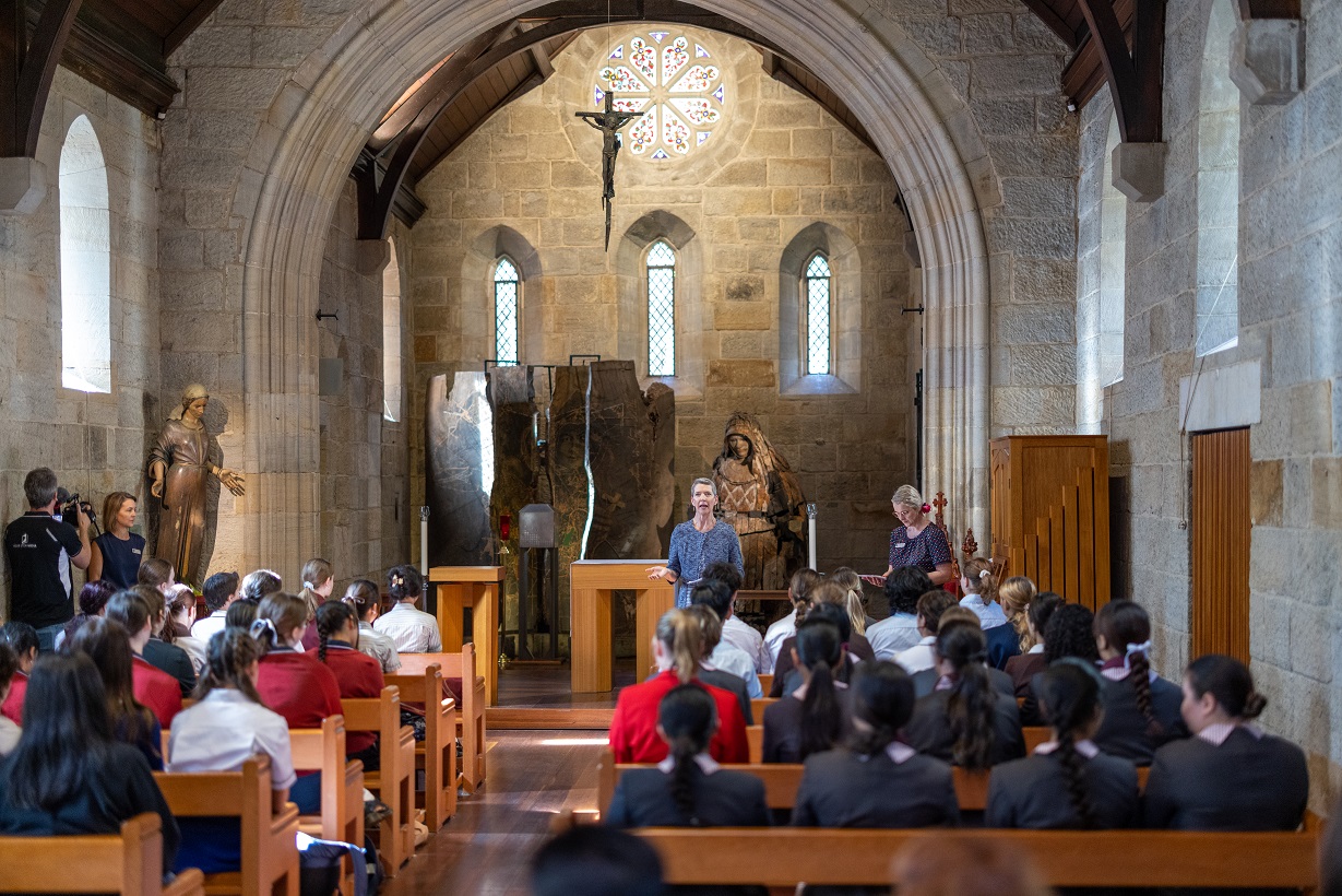 School assembly taking place inside a church with students seated and a speaker at the front.
